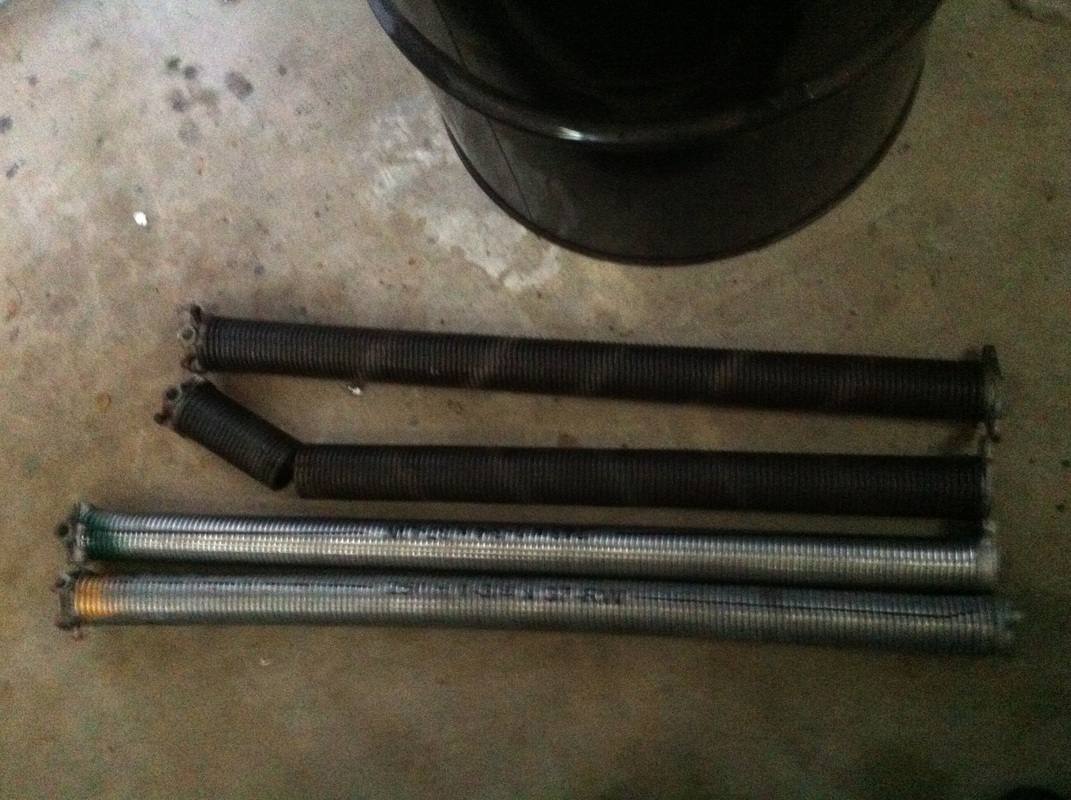 A pair of standard cycle oil tempered torsion springs next to a pair of high cycle galvanized torsion springs